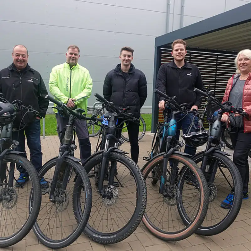 Fünf Hettich Mitarbeitende stehen, bei trübem Wetter, stehen zusammen mit ihren Fahrrädern vor einem Fahrradstand