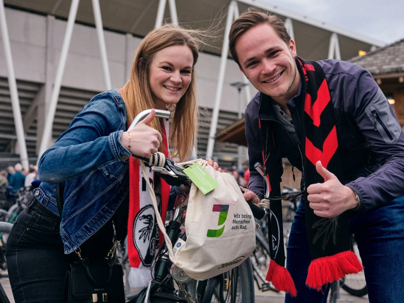 Ein Mann und eine Frau halten eine Goodie Bag am JobRad Aktionsspieltag Klimaschutz und machen beide die Daumen hoch Geste
